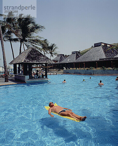 Australien. Queensland. Lindeman Island Resort. Junger Mann entspannt sich auf Lilo im Schwimmbad.