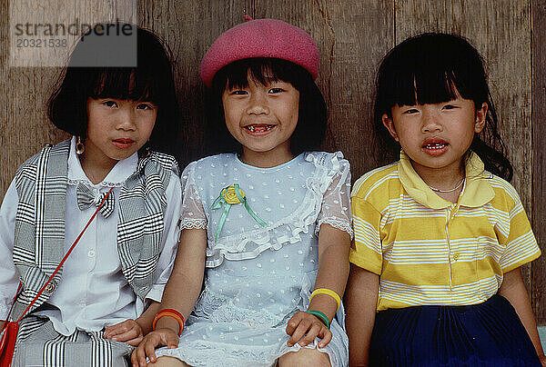 Vietnam. Da Lat. Kinder. Nahaufnahme von drei kleinen Mädchen  die auf einer Bank in einem Holzunterstand sitzen.