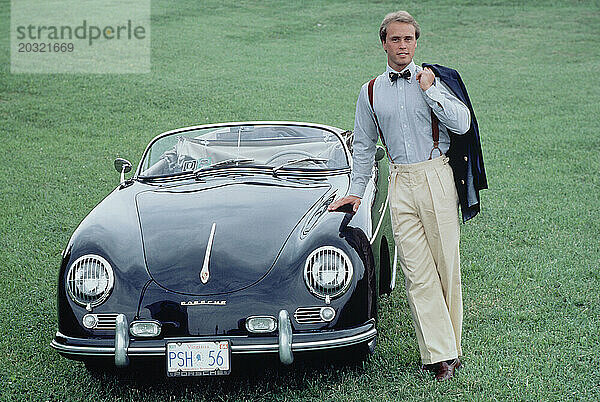 Vereinigte Staaten. Junger Mann steht draußen neben dem klassischen Porsche 356 Cabrio-Sportwagen.