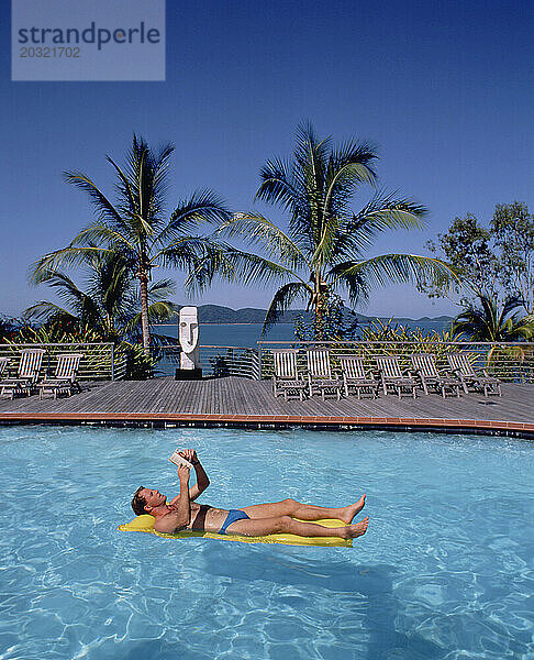 Australien. Queensland. Lindeman Island Resort. Junger Mann entspannt sich auf Lilo im Schwimmbad.