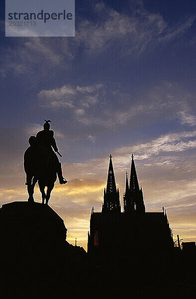 Deutschland. Köln. Silhouetten der Kathedrale und der Reiterstatue Kaiser Wilhelms II. bei Sonnenuntergang.