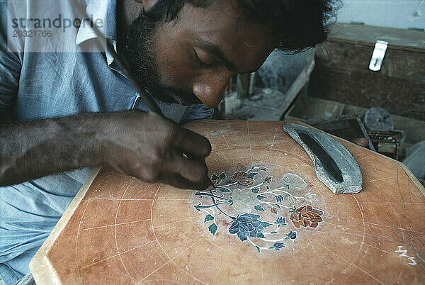 Indien. Neu-Delhi. Kunsthandwerker legt Dekoration auf die Tischplatte.