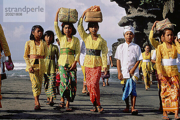 Indonesien. Bali. Hinduistische religiöse Prozession. Frauen und Kinder gehen am Strand entlang.