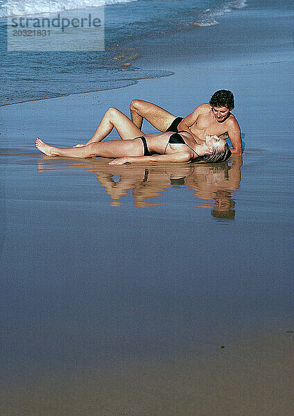 Australien. Queensland. Junges Paar in Badebekleidung liegt am Strand.