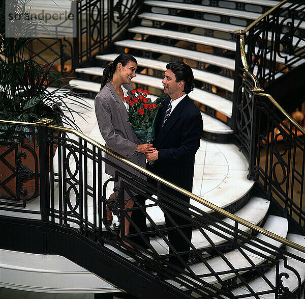 Lebensstil. Junges Paar steht zusammen auf der Treppe. Geschenk aus roten Rosen.