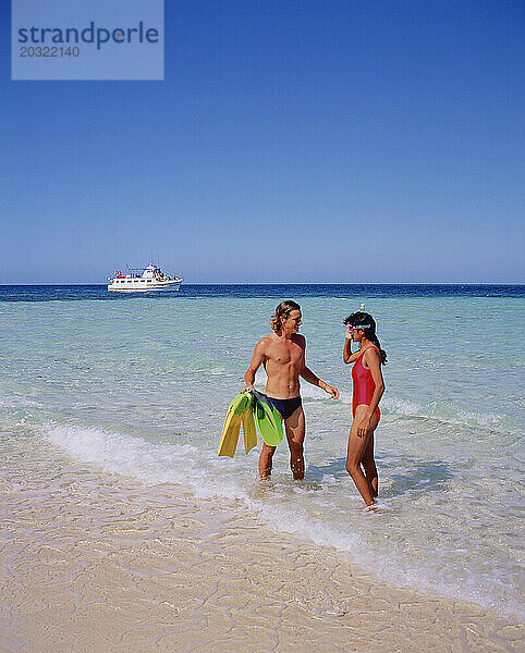 Australien. Queensland. Great Barrier Reef. Junger Mann und junge Frau in Badebekleidung und Tauchausrüstung am Strand.