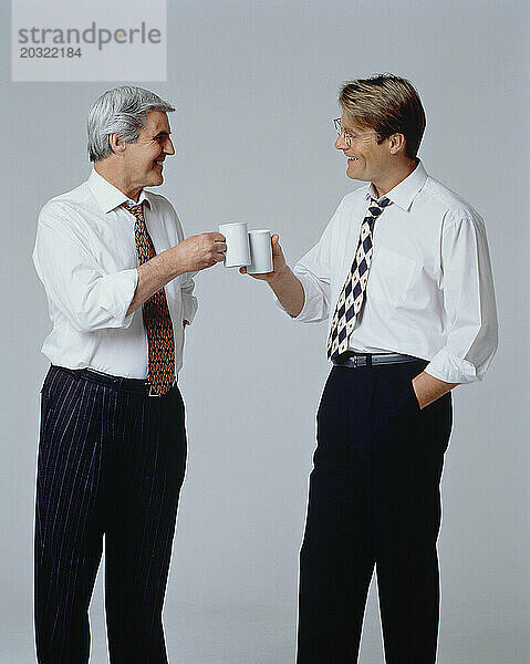 Wirtschaft & Berufe. Zwei leitende Männer in Hemdsärmeln grüßen drinnen mit Kaffeebechern.