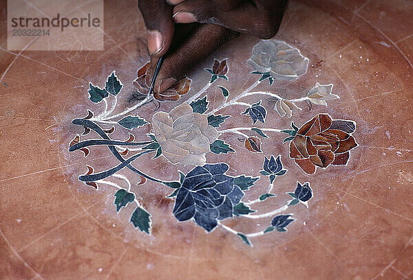 Indien. Neu-Delhi. Nahaufnahme der Hand eines Kunsthandwerkers  der Dekoration auf die Tischplatte legt.