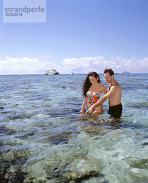 Australien. Queensland. Great Barrier Reef. Junges Paar in Badebekleidung watet im seichten Wasser.