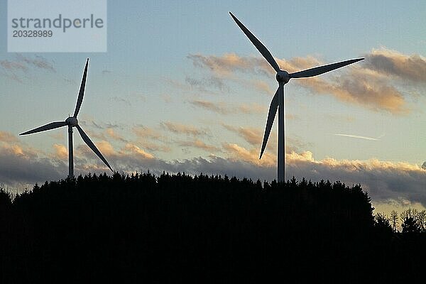 Silhouetten von zwei Windkraftanlagen hinter einem Wald