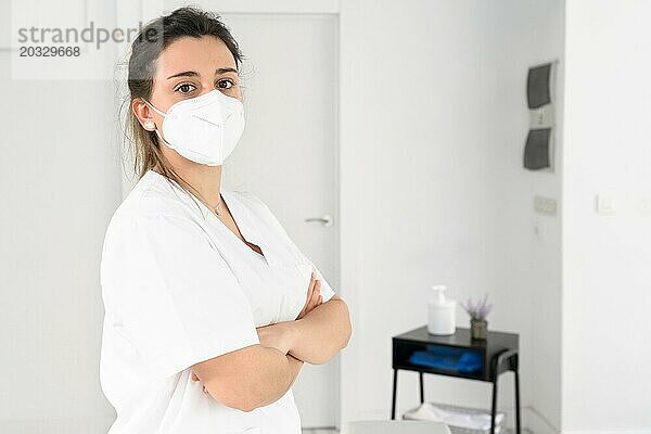 Eine selbstbewusste Physiotherapeutin posiert in einer modernen Klinik und trägt während einer Coronavirus Pandemie eine Schutzmaske. Foto in hoher Qualität