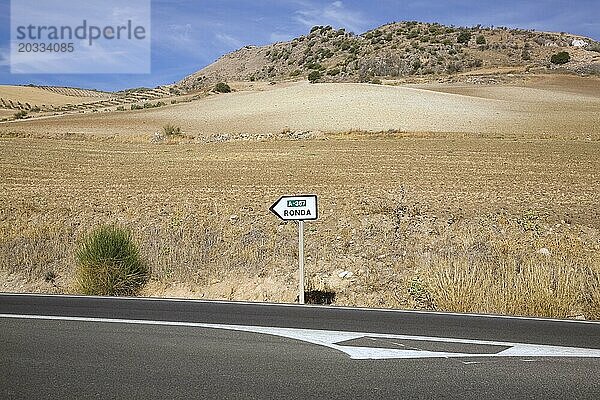 Schwarze Asphaltstraße und Straßenschild inmitten einer trockenen Landschaft  die die Richtung nach Ronda  Spanien  angibt  Europa