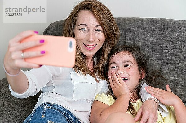 Glückliche Mutter mit ihrer Tochter machen einen Videoanruf zu Vater oder Verwandten in einem Sofa. Konzept der Technologie  neue Generation  Familie  Verbindung  Elternschaft. Hohe Qualität der Fotografie