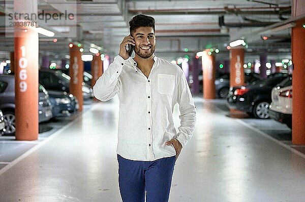 Selbstbewusster  junger  gutaussehender Mann  der auf dem Parkplatz spazieren geht und telefoniert  nachdem er sein Auto geparkt hat. Foto in hoher Qualität