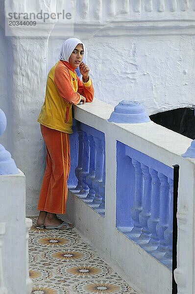 Chefchaouen  Eine Person in traditioneller  farbenfroher Kleidung lehnt nachdenklich an einem Geländer  Chefchaouen  Marokko  Afrika