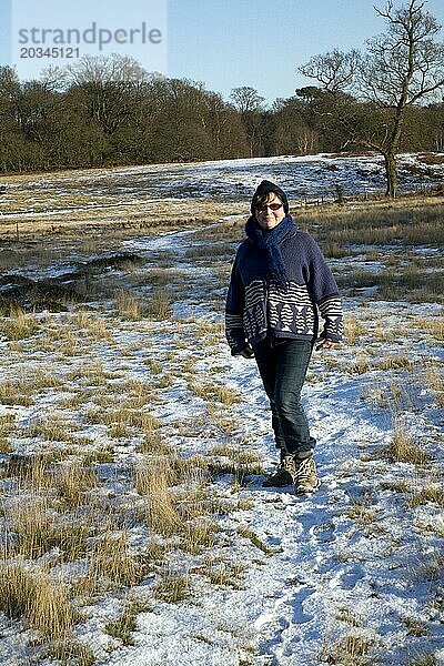 Vorderansicht eines Modells einer reifen Frau  die in einer Heidelandschaft mit Schneedecke steht  Suffolk  England  UK