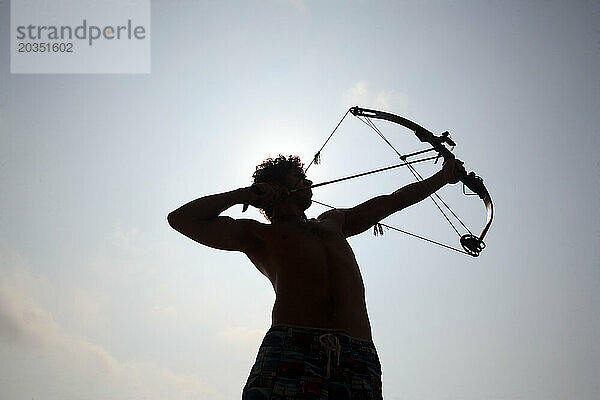 Silhouette eines jungen Mannes beim Bogenschießen auf dem offenen Wasser.