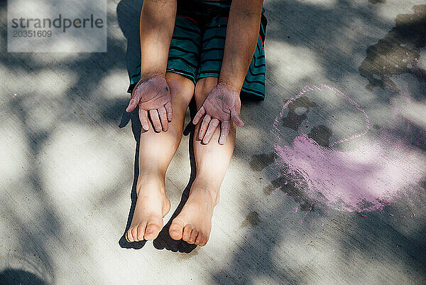 Draufsicht auf einen Jungen mit schmutzigen Händen  der im Sommer mit Kreide spielt