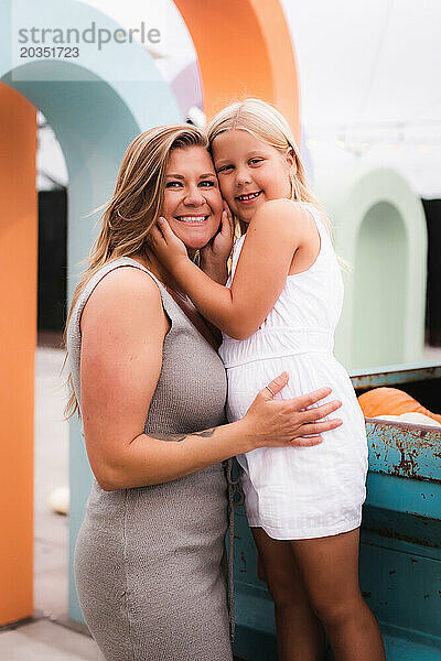 Lächelnde liebevolle Mutter posiert mit Tochter vor buntem Hintergrund