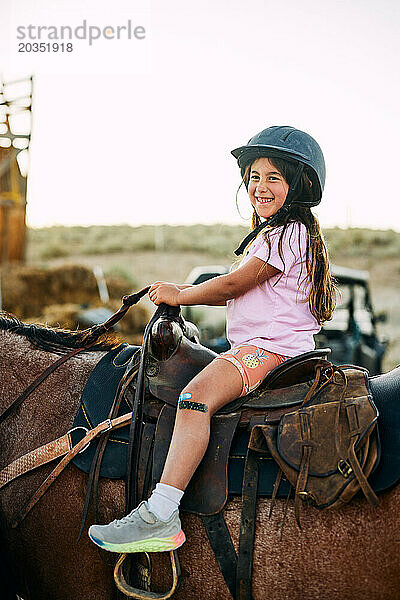 Seitenansicht eines lächelnden Mädchens  das auf dem Pferd auf dem Bauernhof sitzt