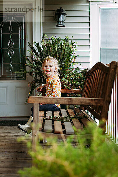 Glückliches junges Mädchen  das im Frühling auf der Verandabank sitzt