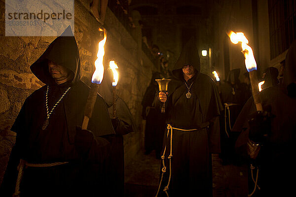 Ein als Benediktinermönch gekleideter Büßer läutet eine Glocke  umgeben von Männern  die Fackeln tragen  bei der Prozession des Schwarzen Christus von Santa Maria während der Karwoche in der Karwoche