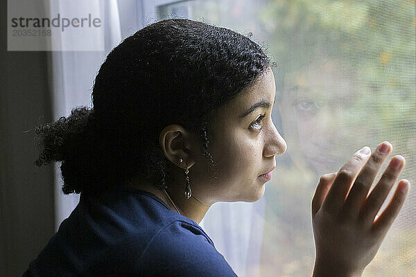 Biracial Teenager-Mädchen im Profil schaut aus einem Fenster