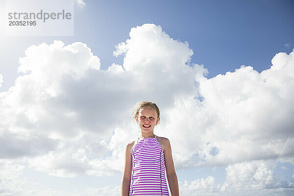 Lächelndes Mädchen in Streifen vor Wolken an einem sonnigen Tag