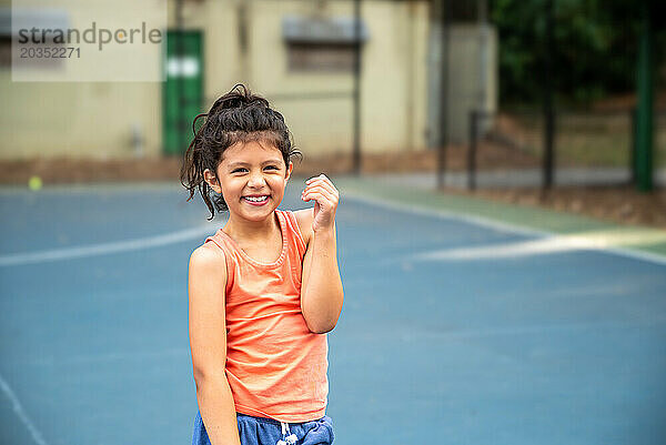 Glückliches Latina-Mädchen lächelt auf dem Tennisplatz