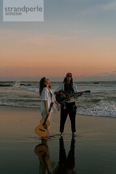 Freundinnen spielen Gitarren am Strand. Sonnenuntergang am Meer. Bali