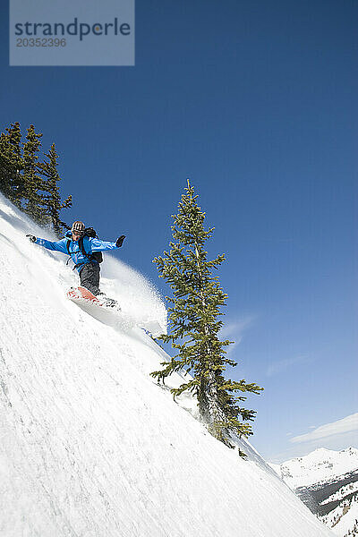 An einem sonnigen Tag in Colorado biegt ein Snowboarder einen steilen Abhang im Hinterland des Mount Axtel hinab.