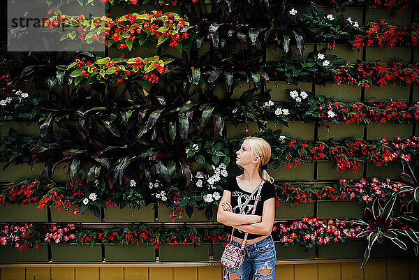 Jugendliches Mädchen blickt im Sommer auf die Blumenwand im Freien