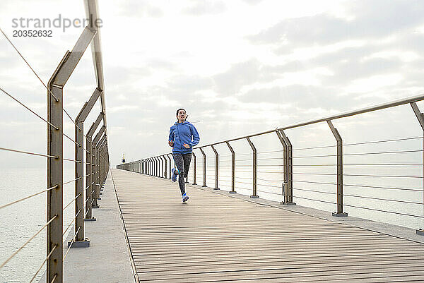 Vorderansicht einer fitten Frau  die auf einer Promenade am Meer läuft