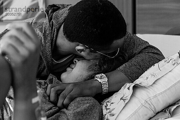 Gemischtrassiges Paar umarmt sich nach der Geburt im Krankenzimmer
