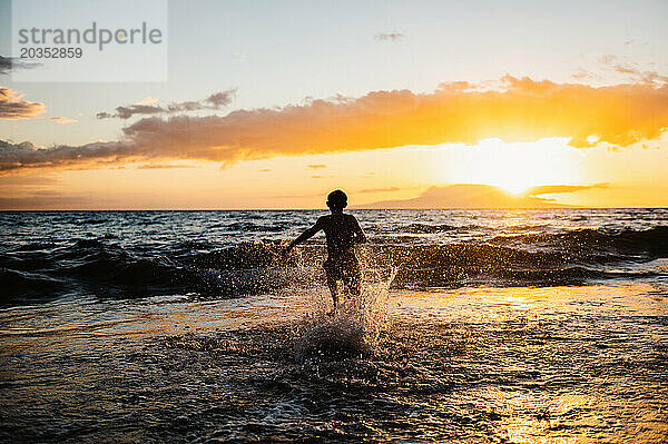 Silhouette eines Kindes  das bei Sonnenuntergang im Meer spielt