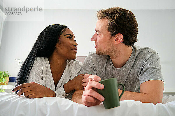 Multiethnisches Paar schaut einander an und lächelt im Bett.