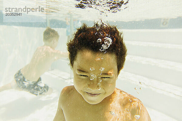 Ein kleiner Junge taucht zusammen mit einem anderen Jungen in einem Schwimmbad unter Wasser.