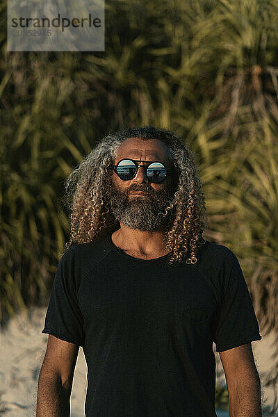 Arabischer Mann  lockiges Haar  Steampunk-Sonnenbrille entspannt am Strand.