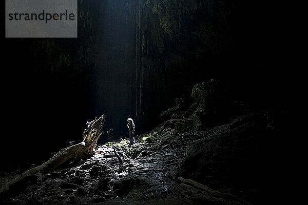 Ein Tourist steht im natürlichen Lichtstrahl  als er die Loltun-Höhlen auf der Halbinsel Yucatan in Mexiko besucht.