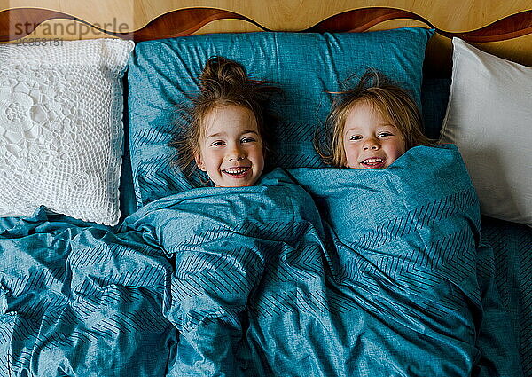 Zwei kleine lächelnde süße Schwestern liegen im Bett  Draufsicht.