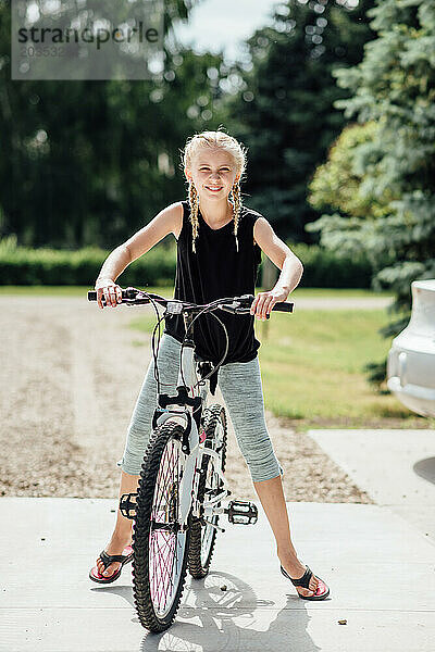 Vorderansicht eines jugendlichen Mädchens  das auf dem Fahrrad steht und im Garten lächelt