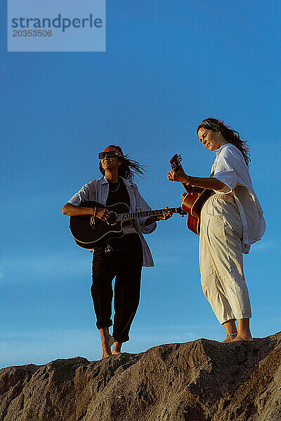 Freundinnen spielen Gitarren am Strand. Sonnenuntergang am Meer. Bali