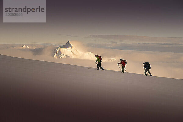 Drei Skibergsteiger besteigen den Denali  im Hintergrund der Sonnenuntergang über dem Mount Hunter.