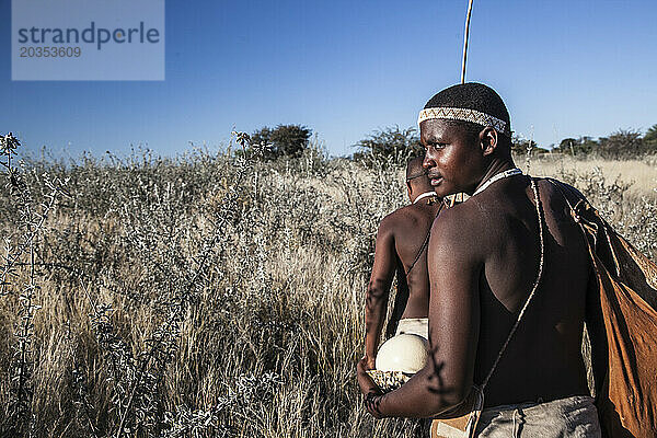 Zwei Mitglieder des San-Volkes gehen durch Unterholz in der Kalahari-Wüste  Botswana