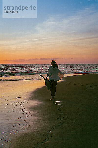 Musikerin mit Gitarre am Strand bei Sonnenuntergang. Bali