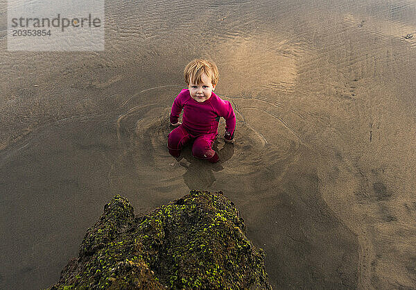 Ein Kleinkind spielt im seichten Wasser am Strand.