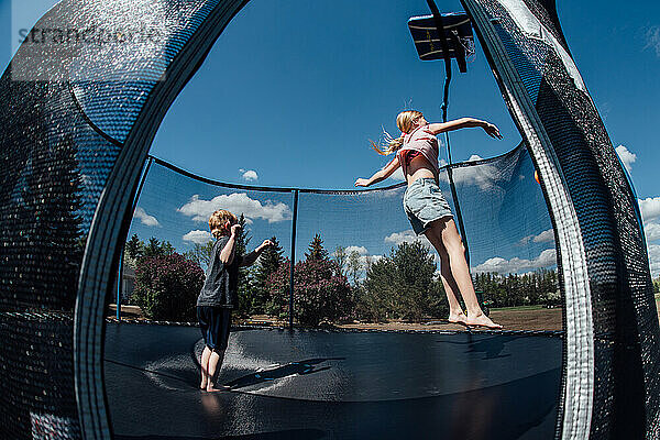 Zwei Kinder springen im Sommer draußen auf dem Trampolin.