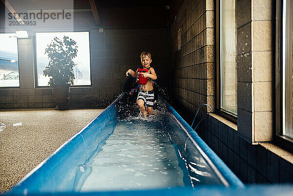 Kleiner Junge läuft drinnen im Wasserpark durch Wasser