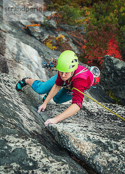 Frau klettert während der Laubsaison mit traditioneller Ausrüstung auf Felswand