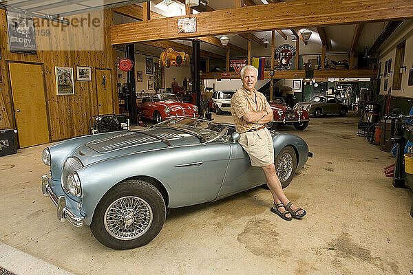 Ein Mann posiert mit seiner Sammlung antiker Sportwagen für ein Porträt in seiner Garage.
